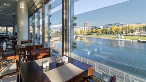 Een modern restaurant met grote ramen met uitzicht op een rivier en een stadsbeeld.