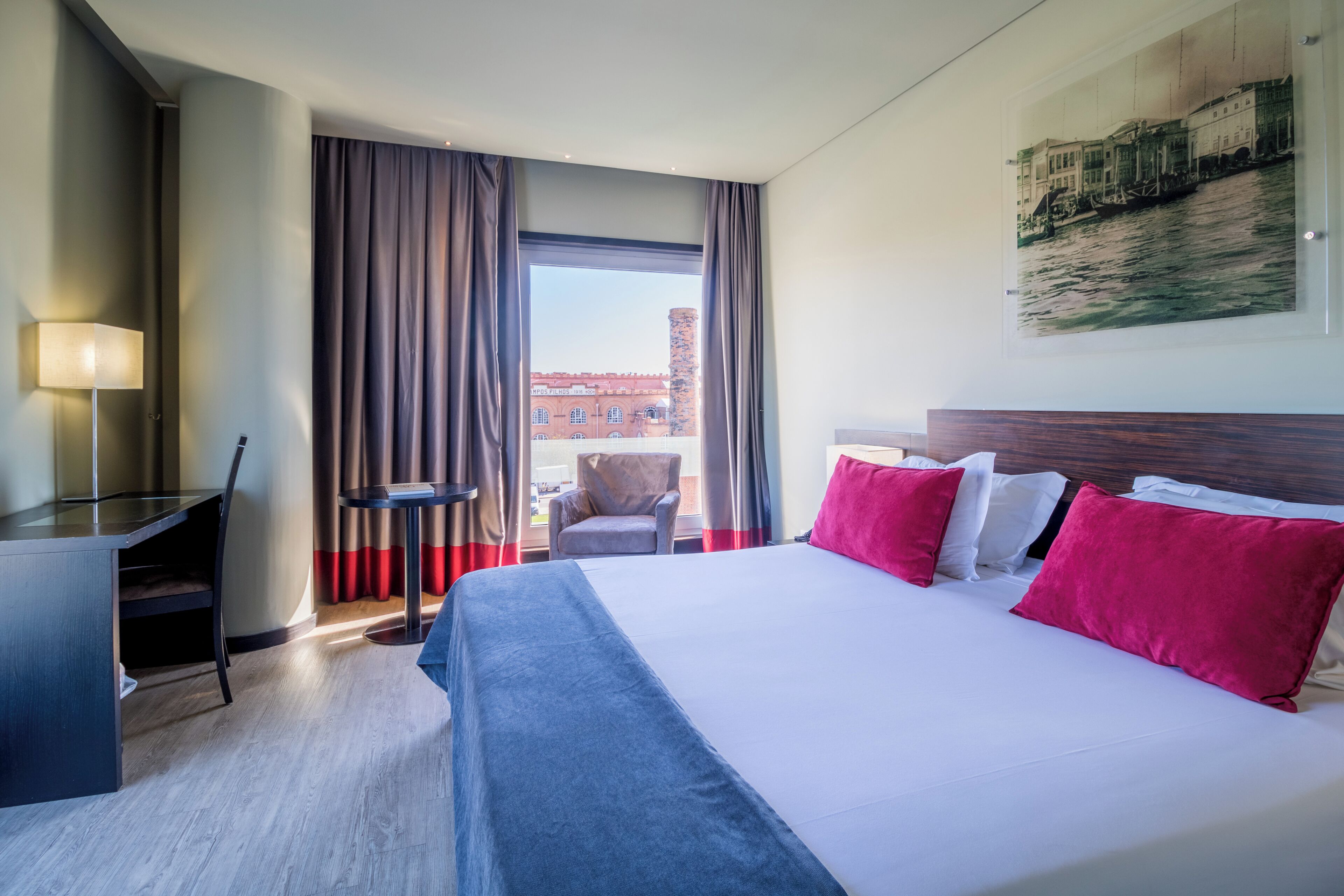 Habitación de hotel con cama, escritorio, silla y vista a un edificio a través de una ventana.