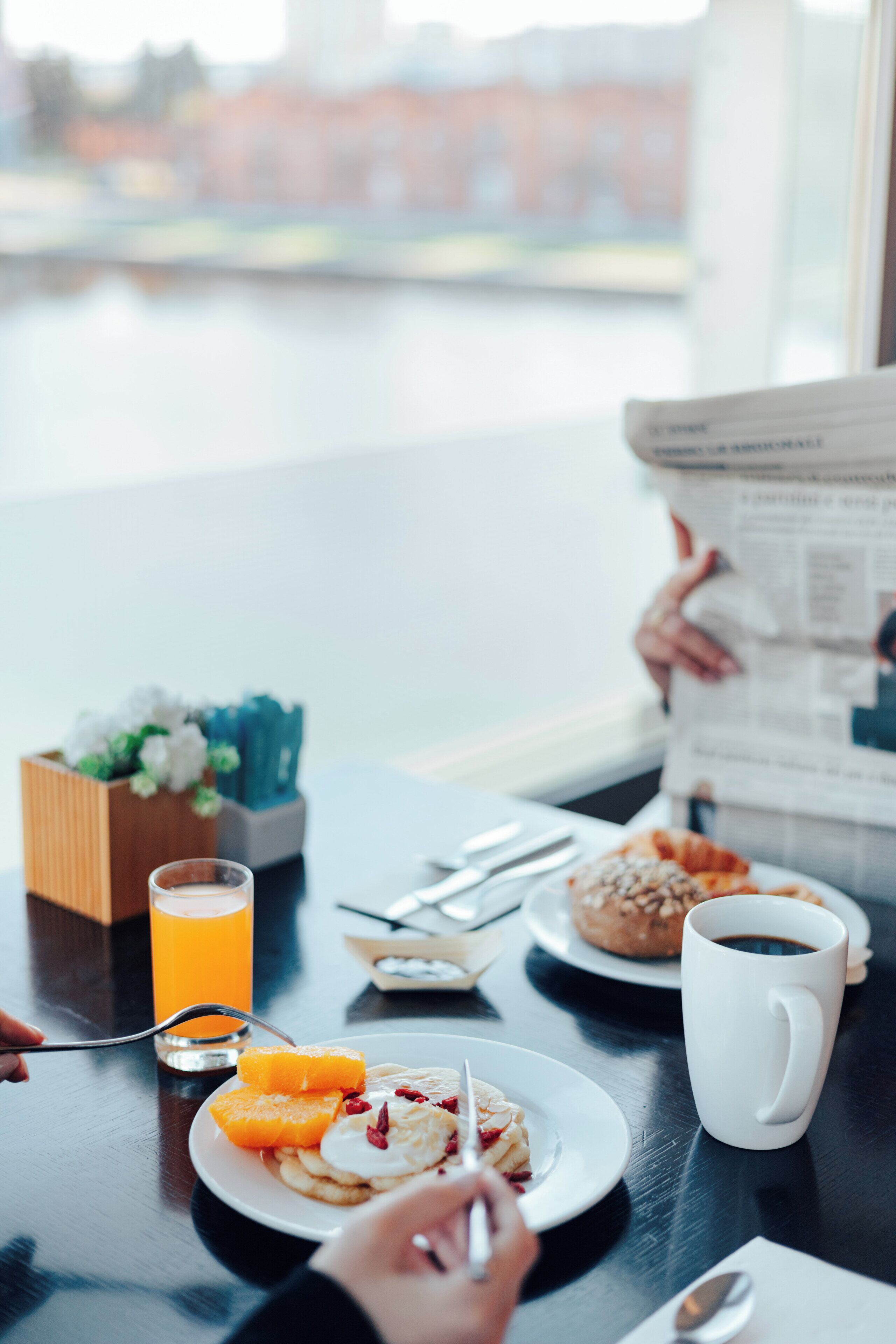 A breakfast setting with a plate of food, a glass of orange juice, a mug, and a newspaper.