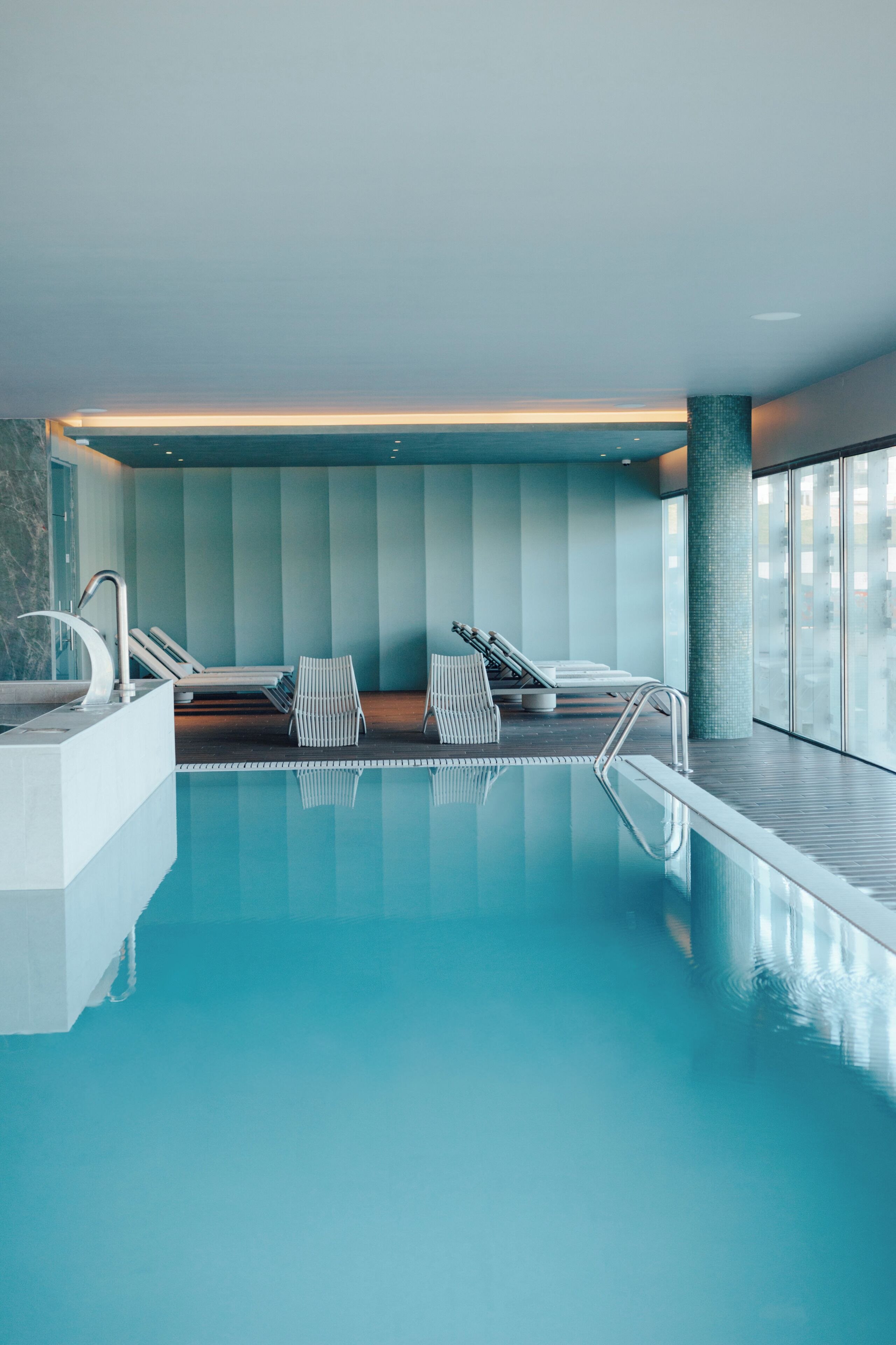 An indoor swimming pool with clear water, lounge chairs, and a modern design.