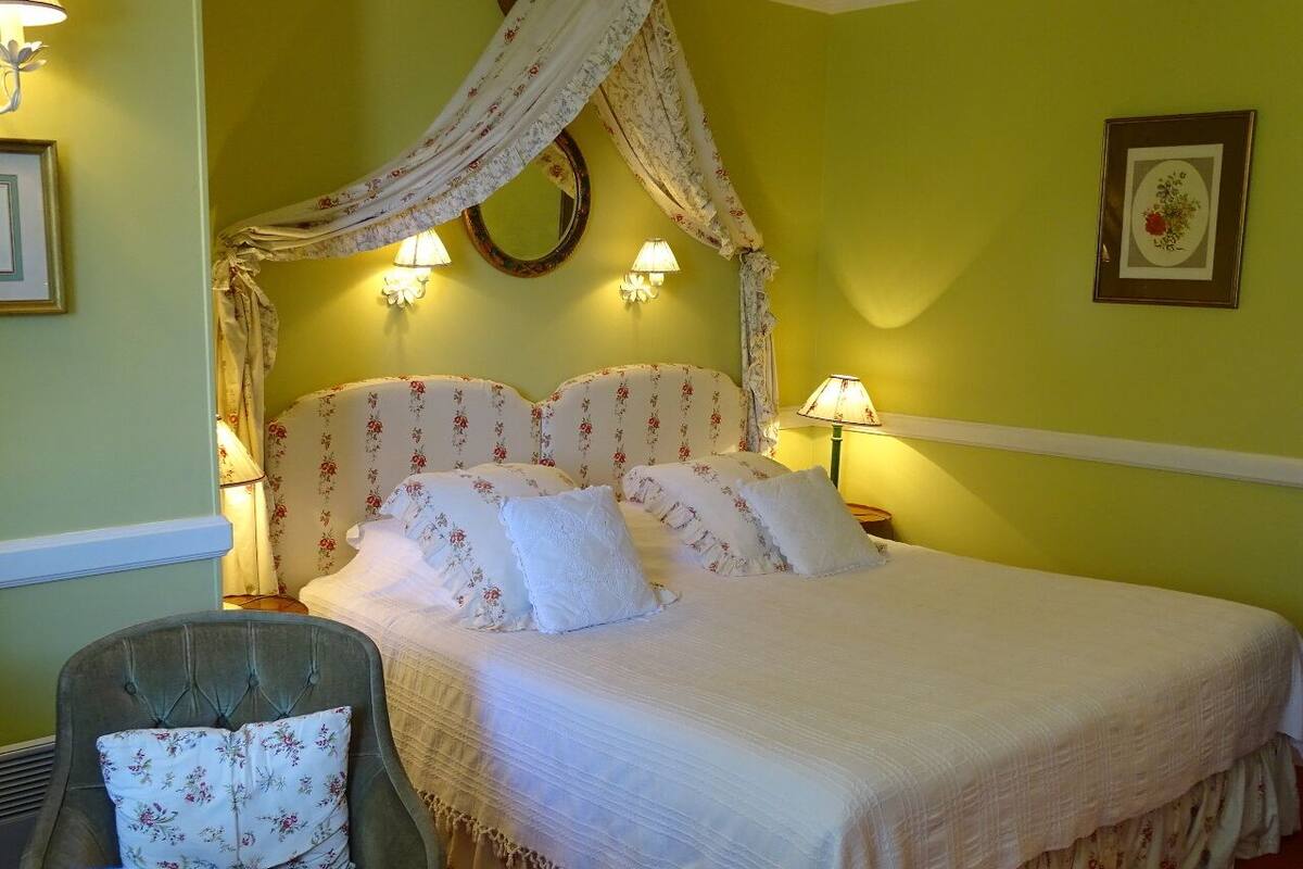 A bedroom with a canopy bed, floral-patterned bedding, and wall-mounted lamps.