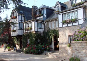 Un edificio tradicional de estilo Tudor con fachada de piedra, múltiples ventanas y un jardín bien cuidado con plantas en flor.