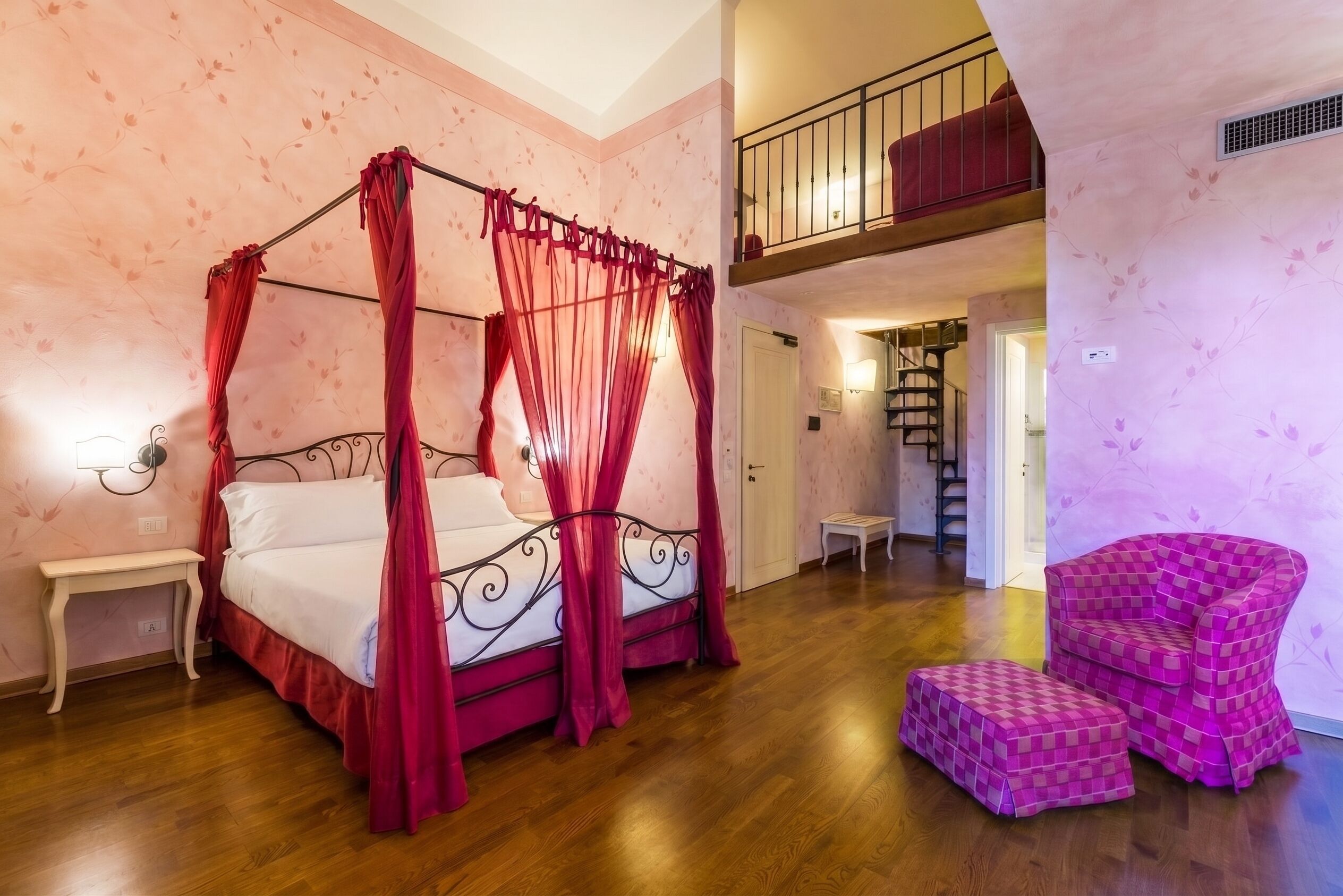 Ein Schlafzimmer mit einem Himmelbett, einem Nachttisch, einem Sessel und einer Treppe, die zu einer oberen Ebene führt.