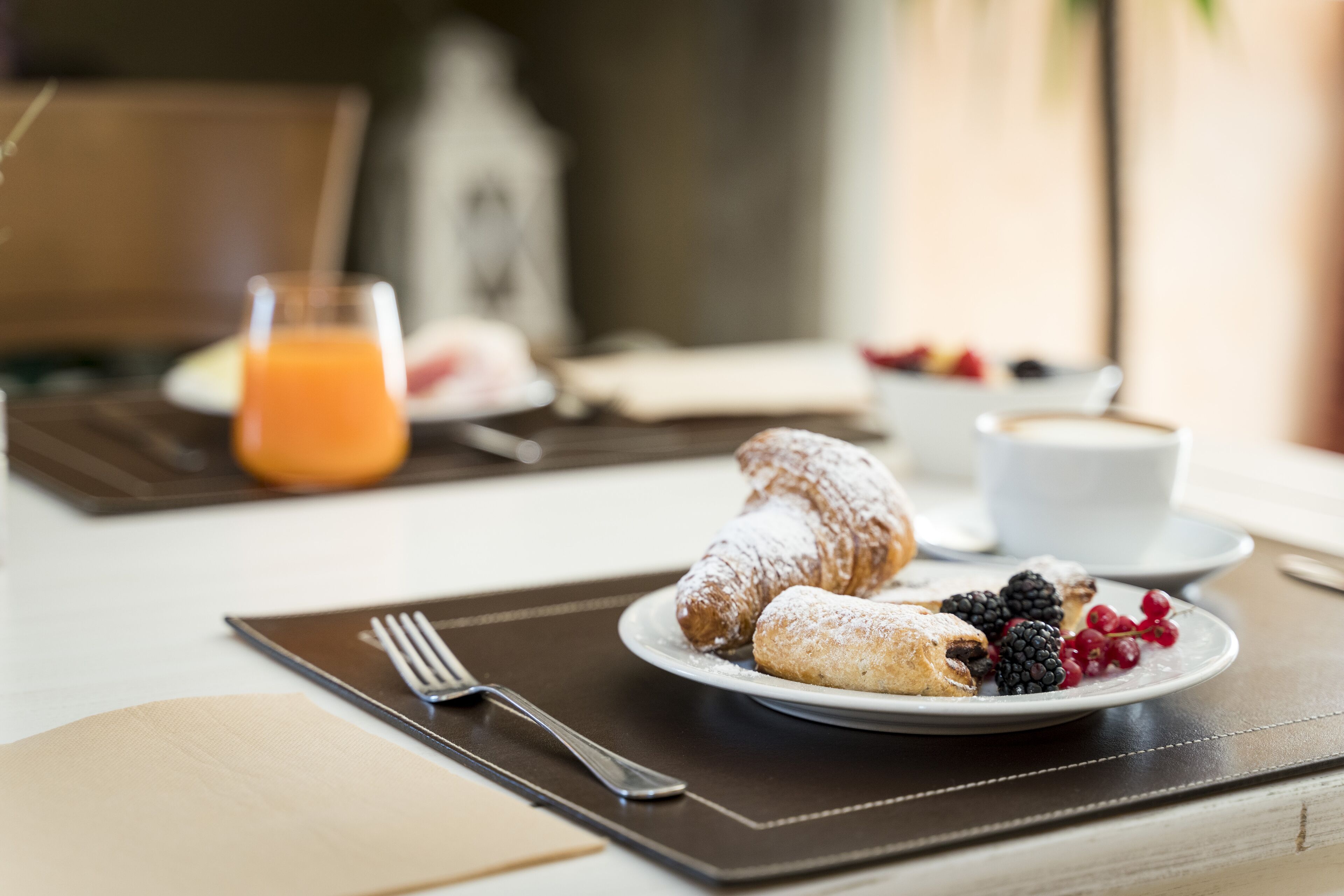 Una mesa con un croissant, bayas y un vaso de jugo de naranja para el desayuno.