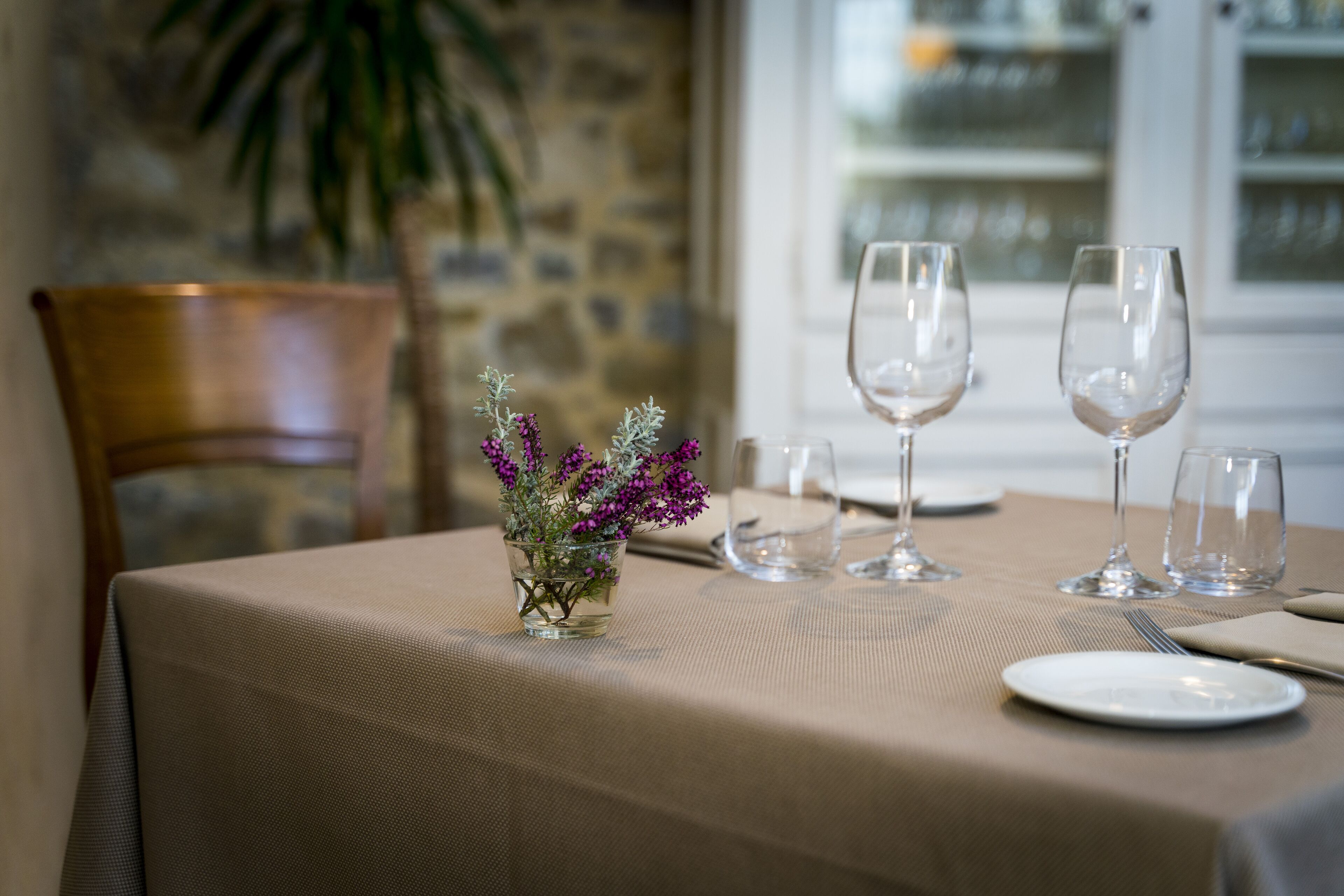A dining table set with a vase of purple flowers, empty wine glasses, and a white plate.