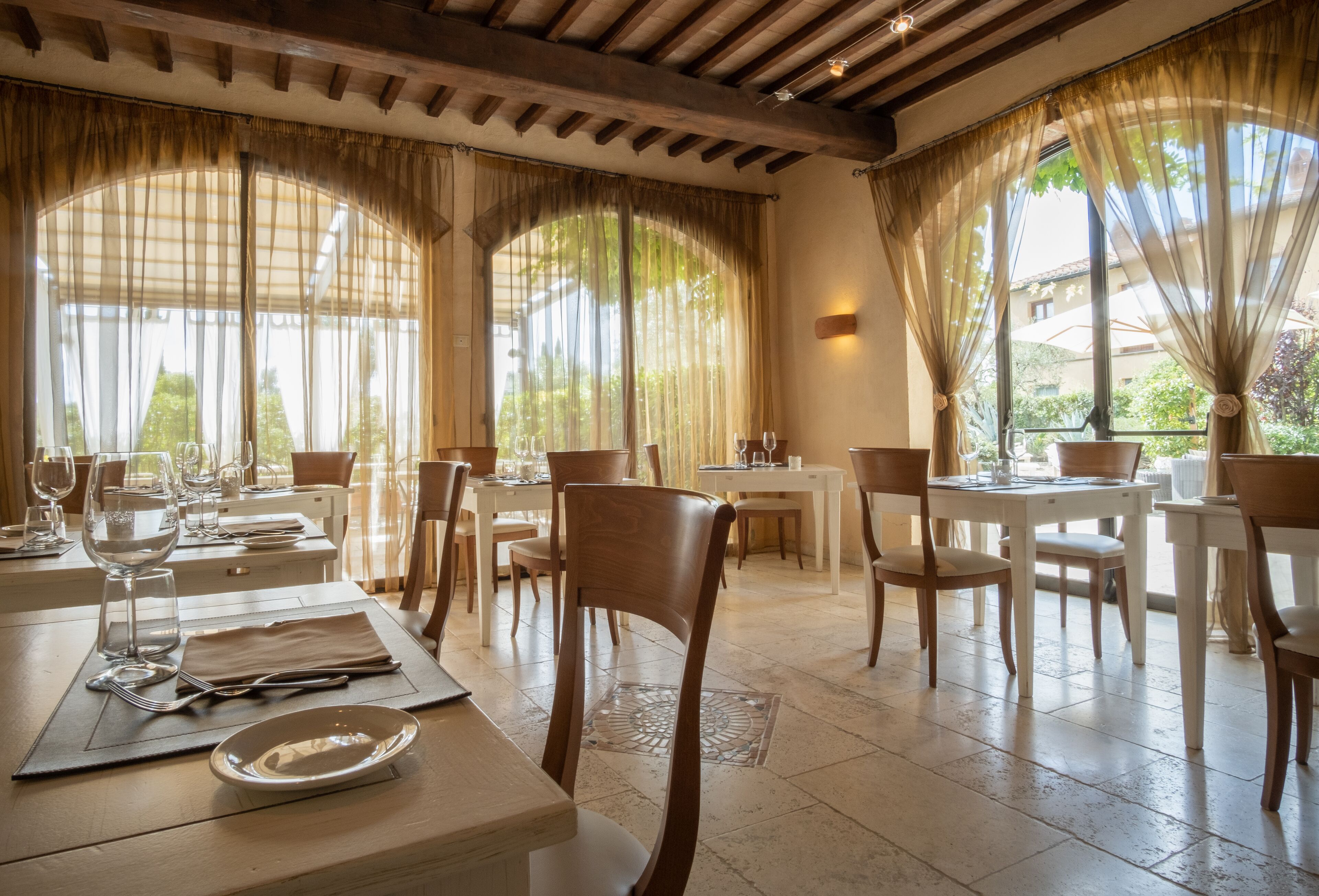 Un comedor con mesas dispuestas para una comida, sillas y vistas al exterior a través de amplios ventanales.