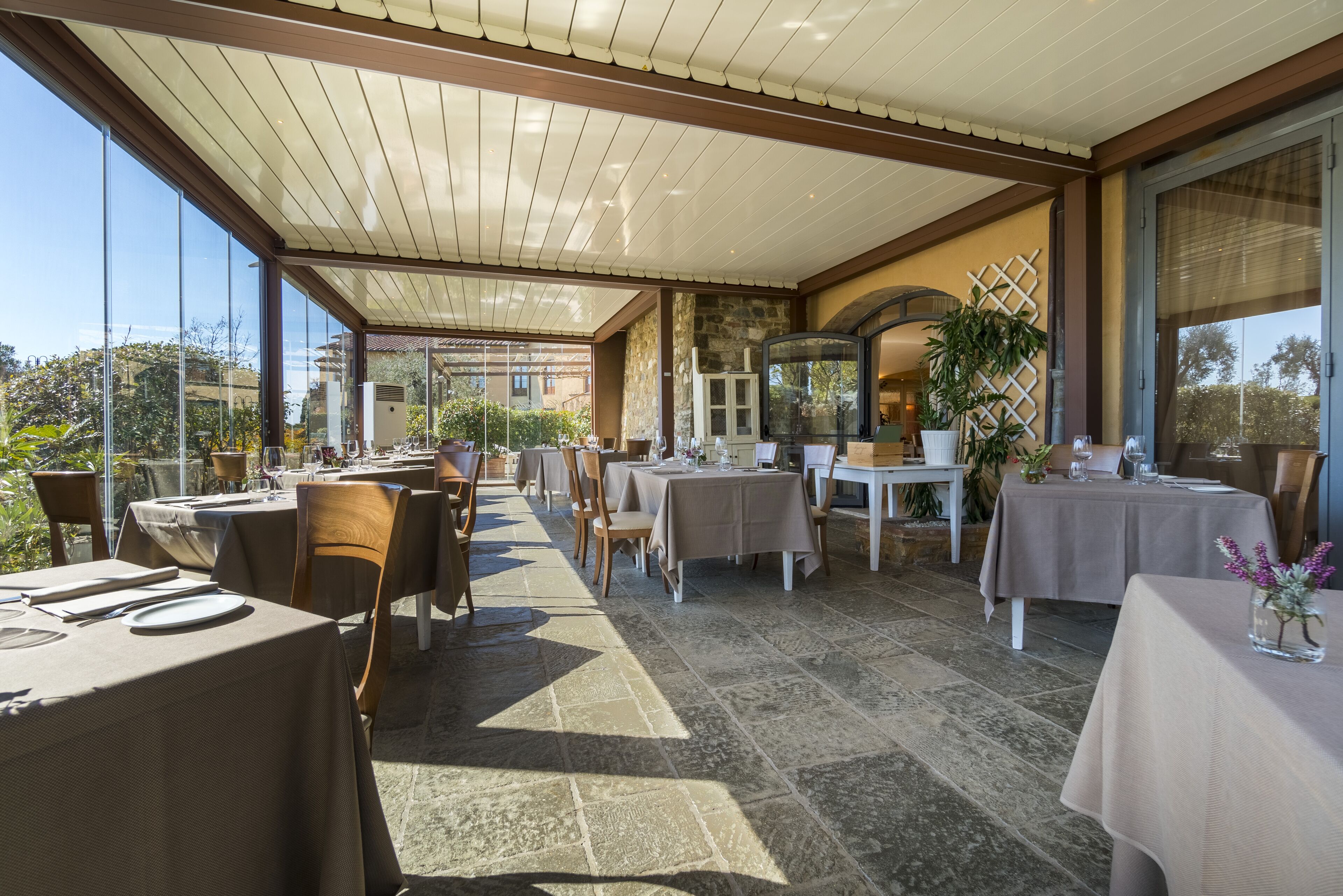 An outdoor dining area with tables and chairs, a stone floor, and a view of the surrounding buildings.