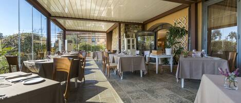 An outdoor dining area with tables and chairs, a stone floor, and a view of the surrounding buildings.