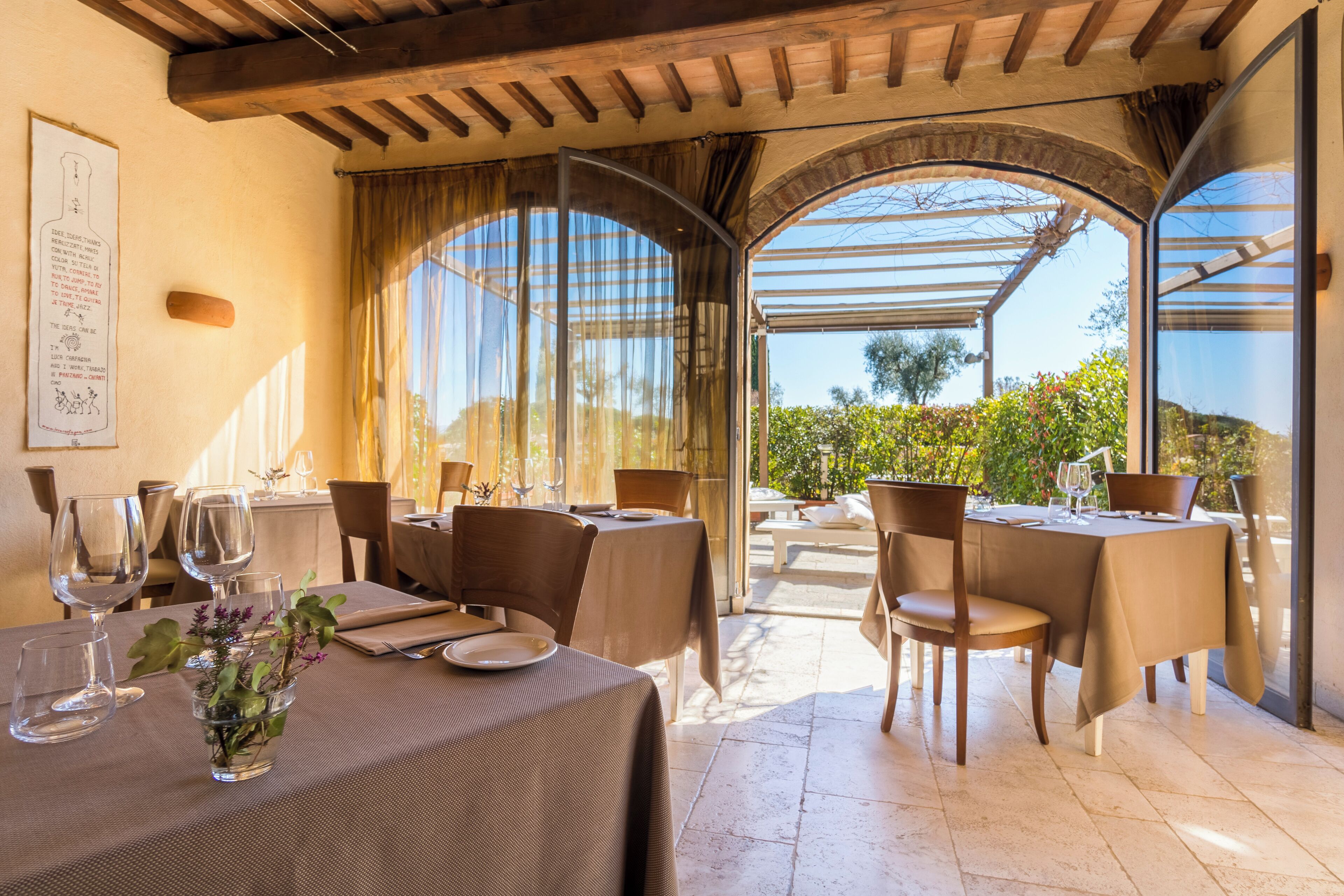 A restaurant with tables set for dining, large windows, and a view of greenery.
