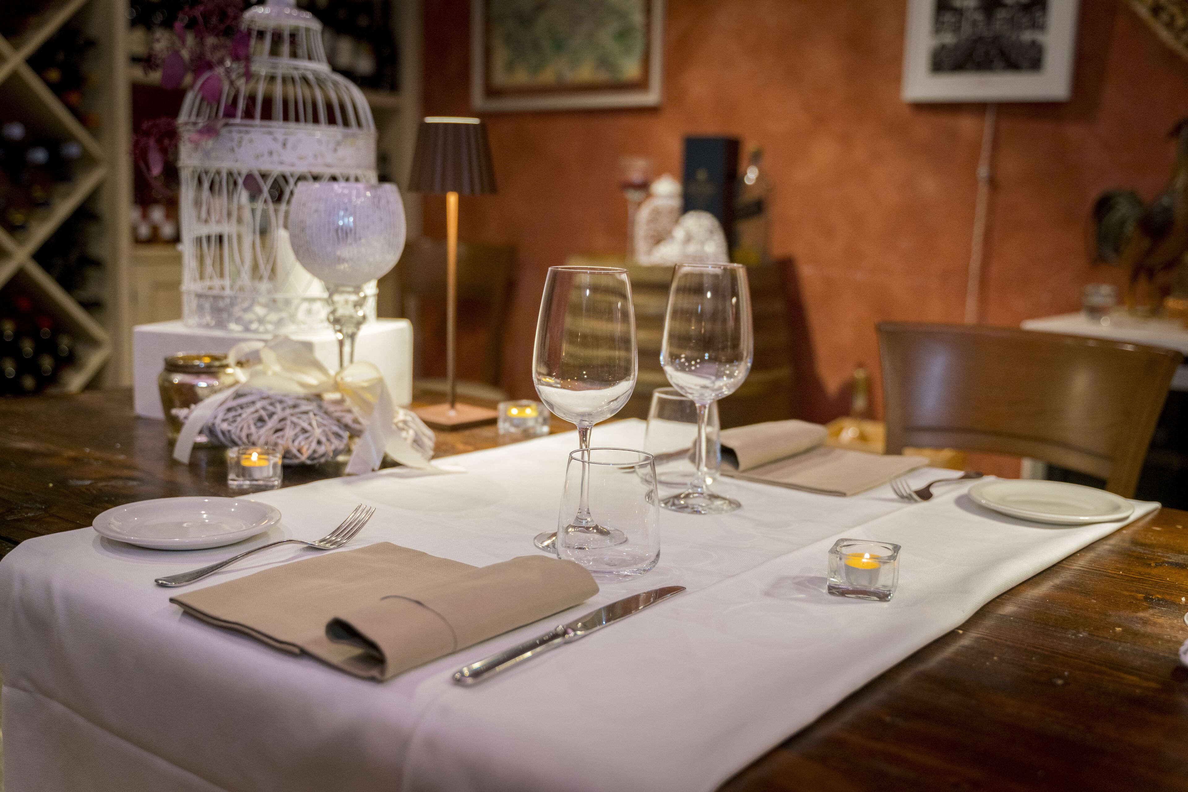 A dining table set with white tablecloth, plates, cutlery, and two wine glasses.