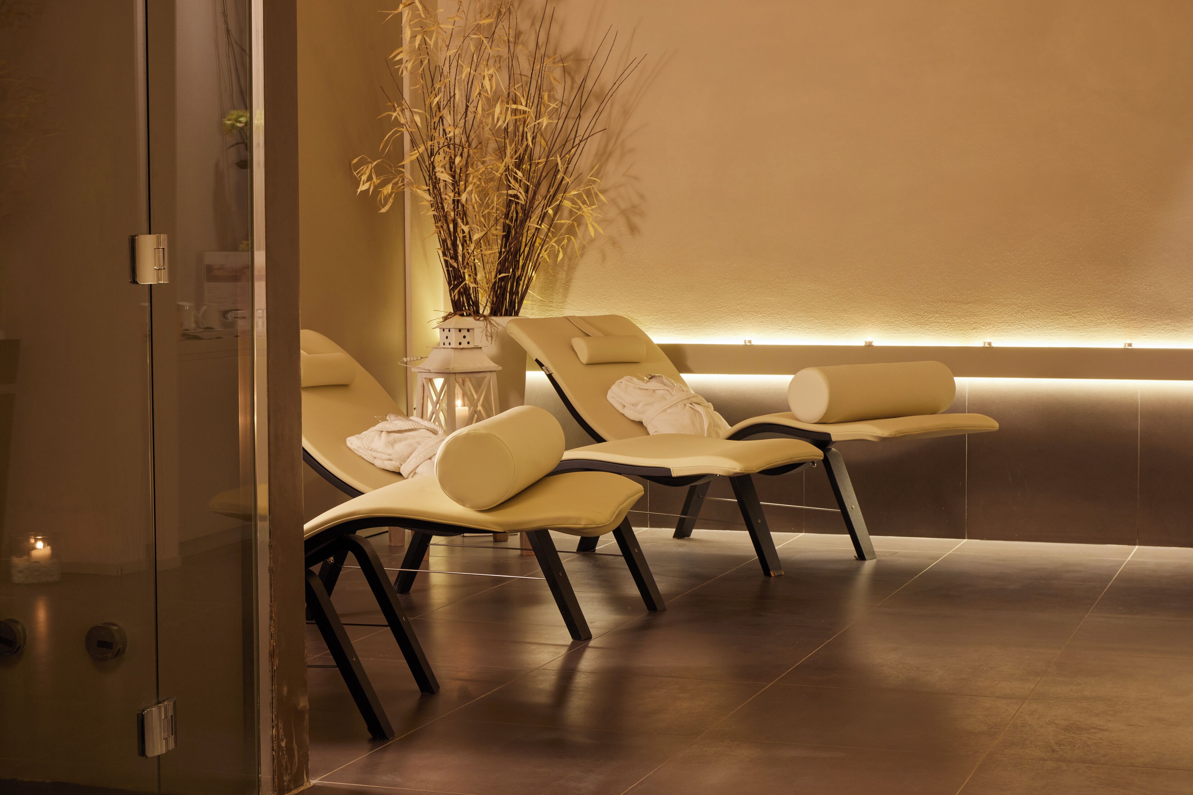 A spa area with three reclining chairs, a vase with dried plants, and a wall-mounted light fixture.