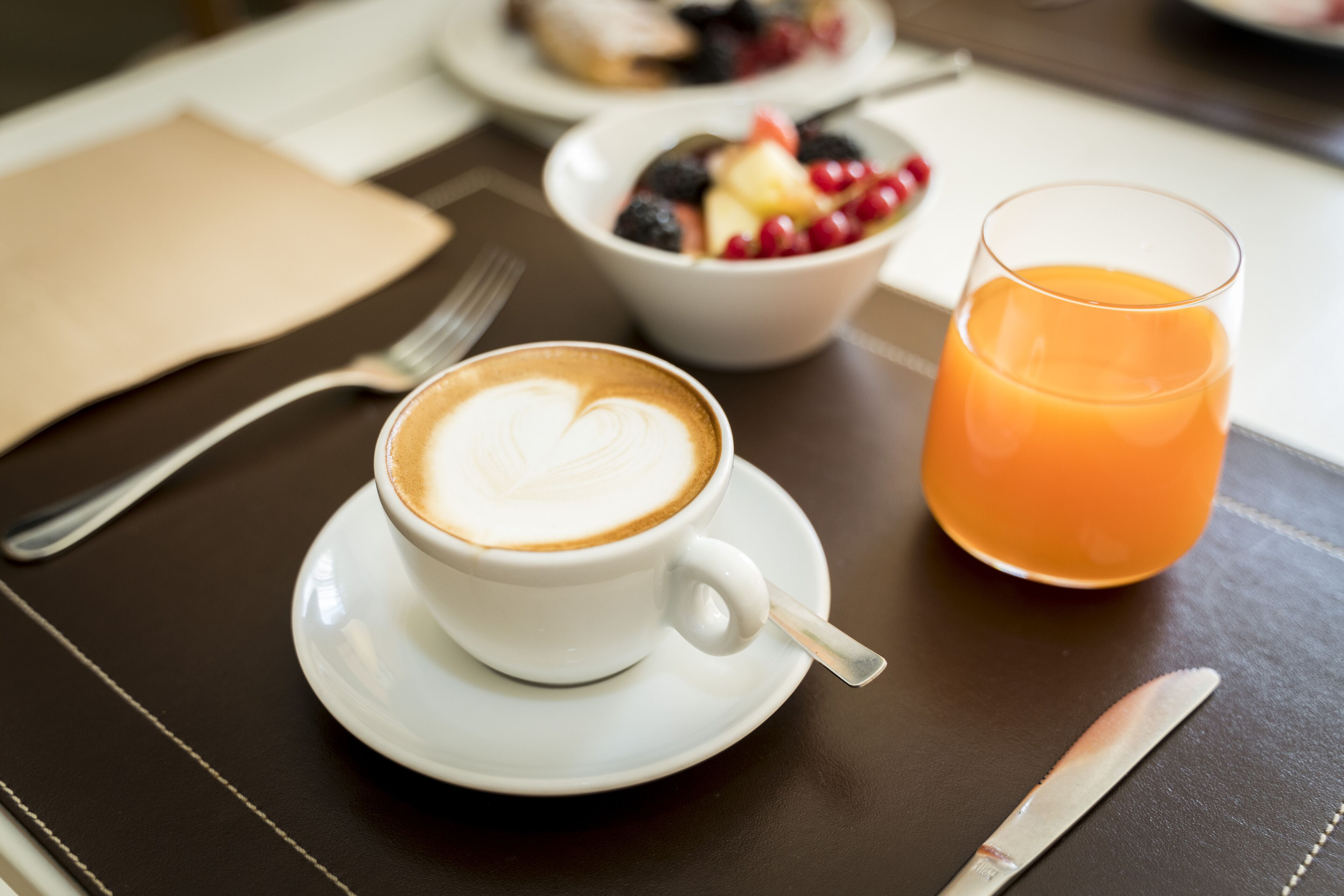 Et bord med en hvid kaffekop, et glas appelsinjuice og en skål med frugt.