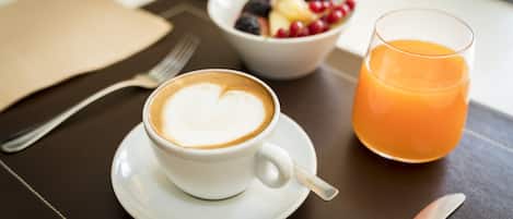 A table with a white coffee cup, a glass of orange juice, and a bowl of fruit.
