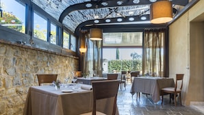Un comedor interior con paredes de piedra, mesas dispuestas con manteles y sillas, e iluminación colgante.