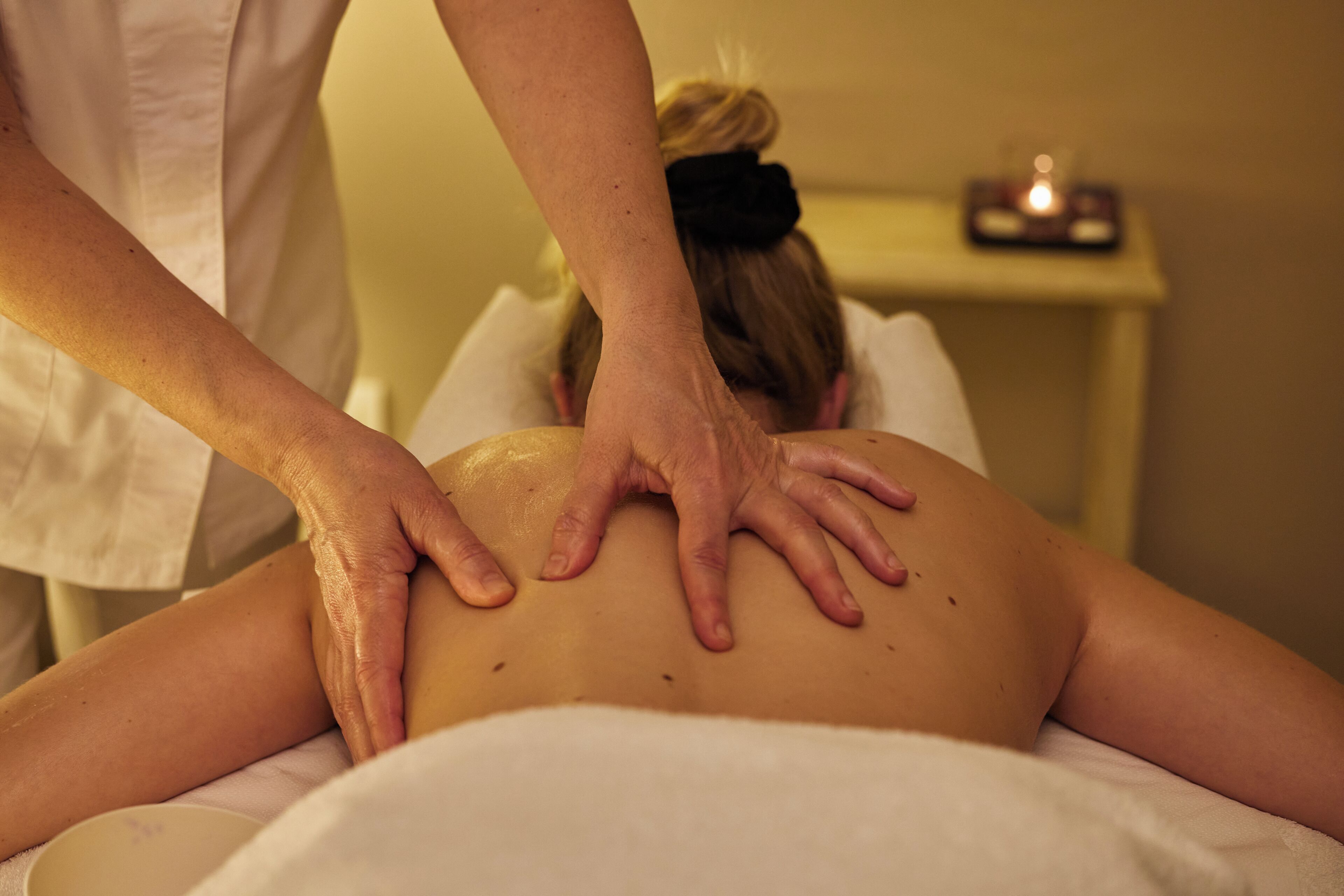 A person receiving a back massage in a room with a small table and a candle in the background.