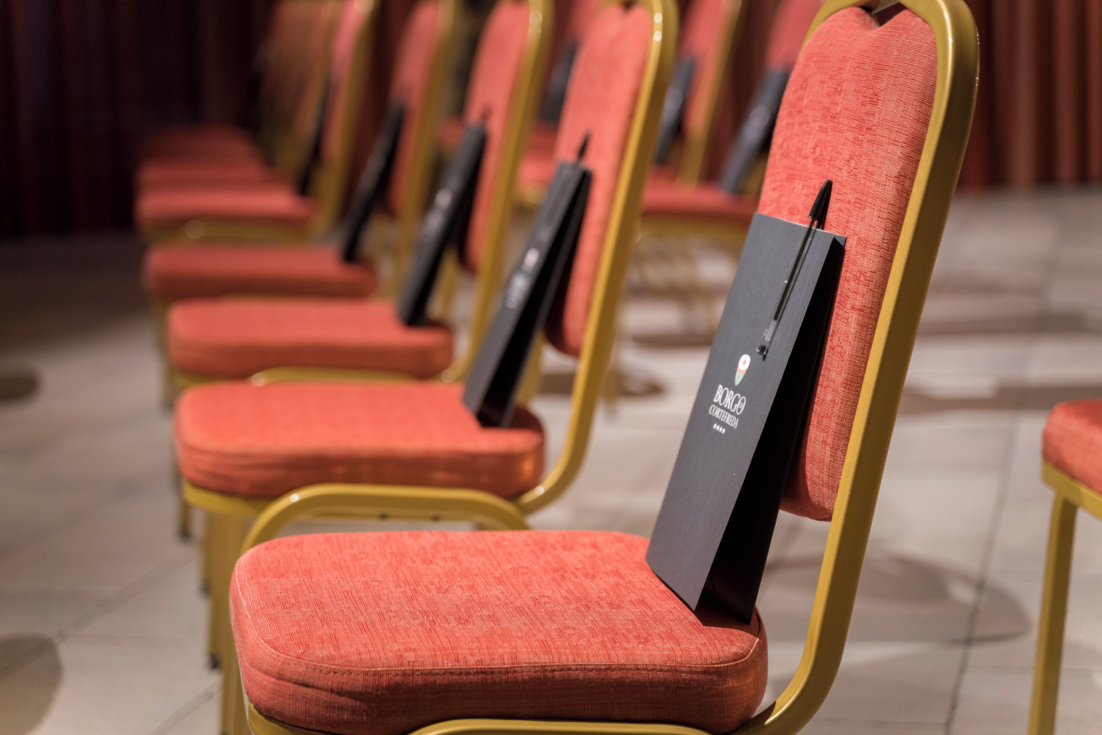 Rows of red upholstered chairs with gold frames, arranged in a theater-style seating layout.