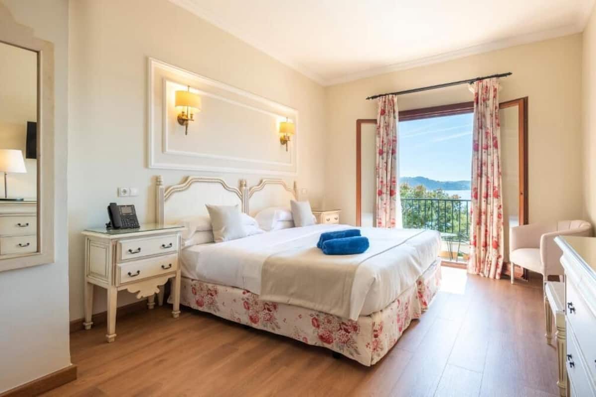 A bedroom with a bed, bedside tables, a telephone, and a view of the outdoors.
