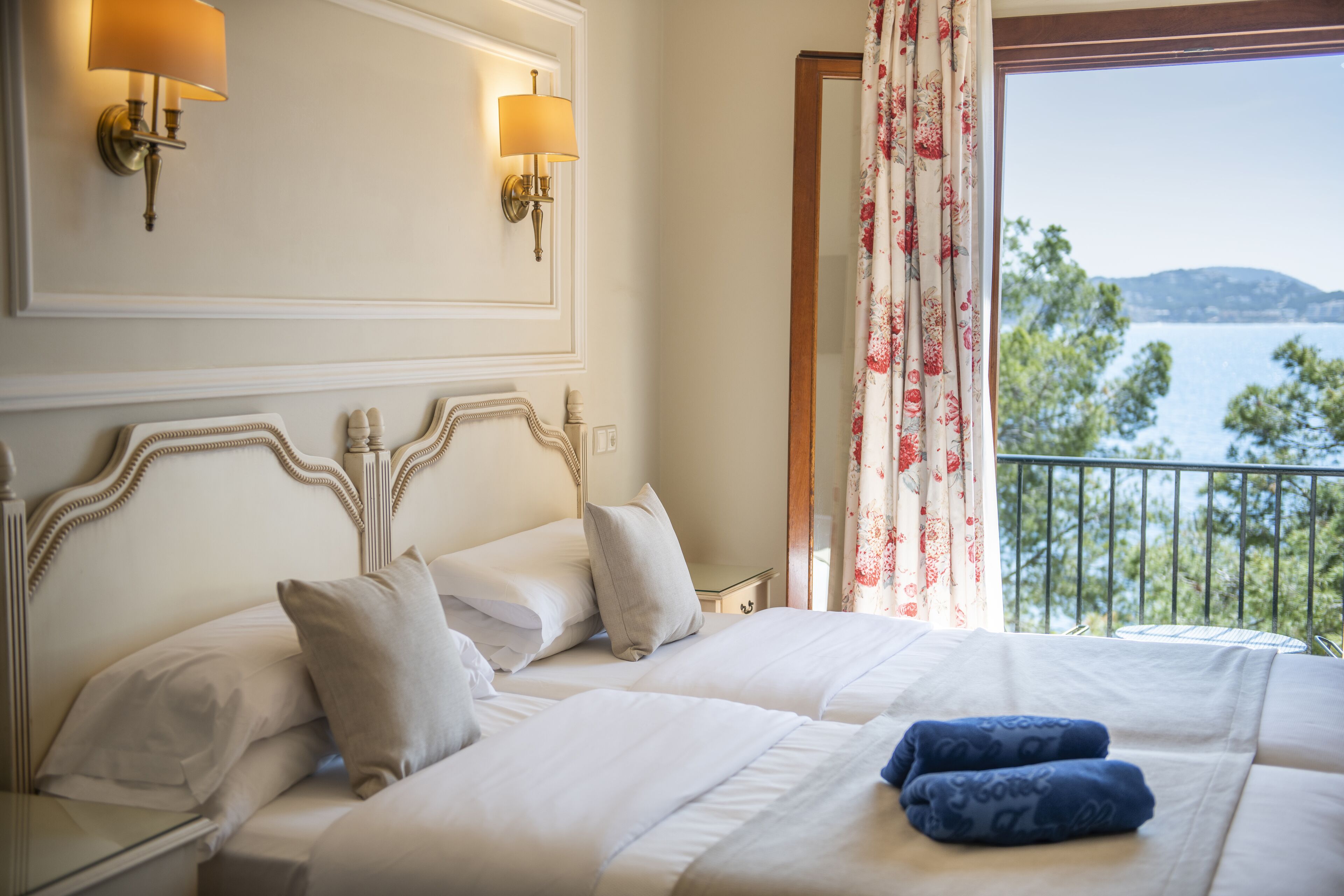A hotel room with a large bed, two wall-mounted lamps, and a view of a body of water through a balcony.