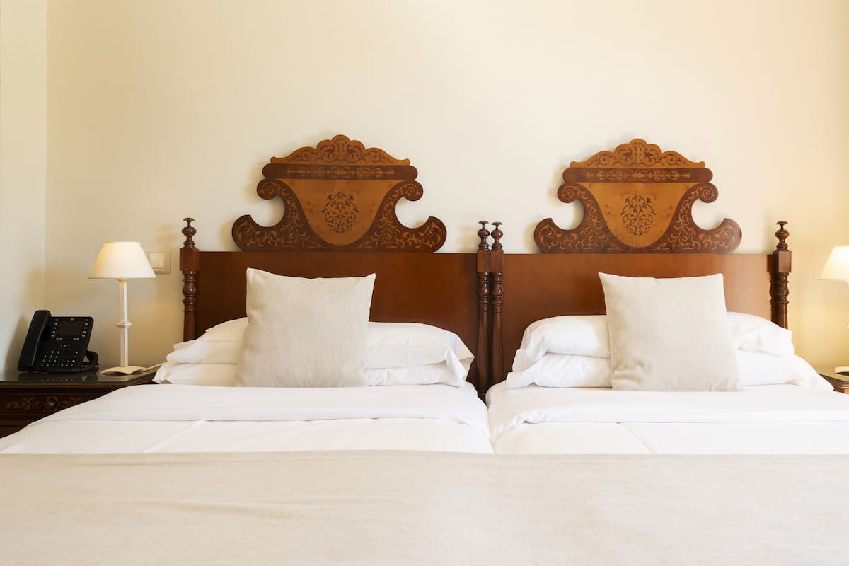 A double bed with a wooden headboard, white bedding, two bedside tables with lamps, and a telephone on the left table.