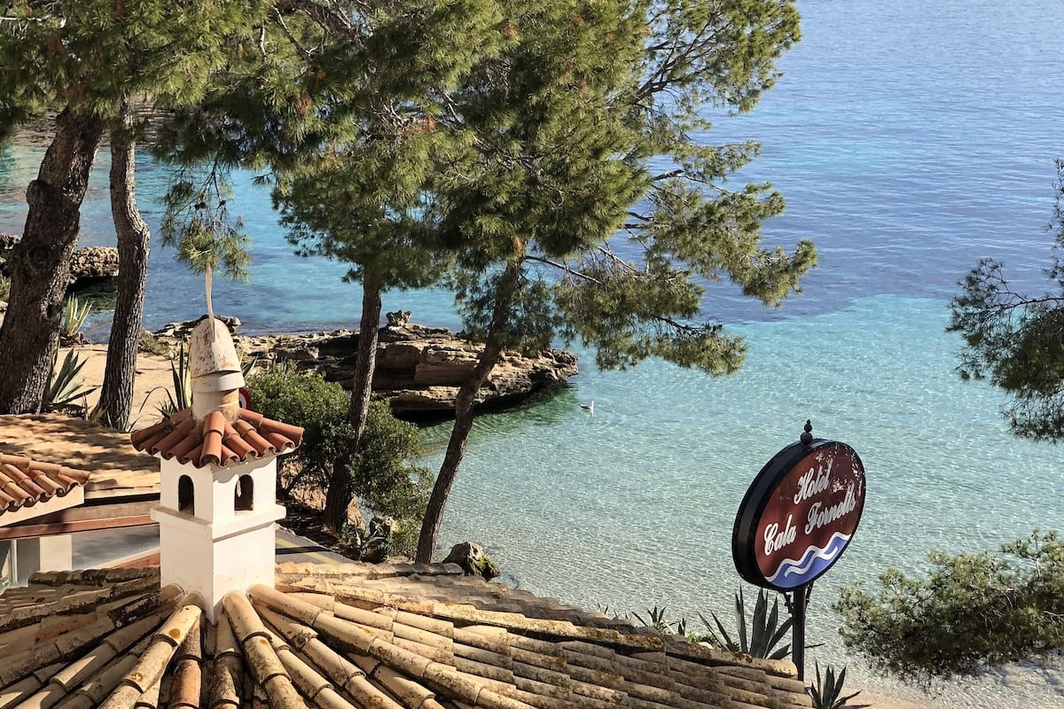 A coastal view with a clear sky, a beach, and a sign for "Hotel Cala Fornelli."