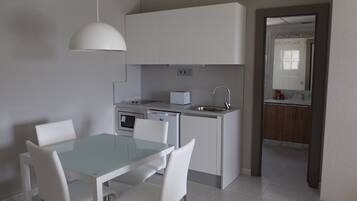 Una cocina moderna con armarios blancos, horno empotrado y un lavabo. Hay una mesa de comedor con sillas y una lámpara colgante arriba.