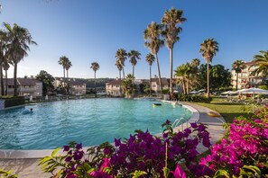 Une piscine entourée de palmiers et un jardin agrémenté de fleurs violettes.