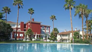 A hotel with a swimming pool, palm trees, and a red building.