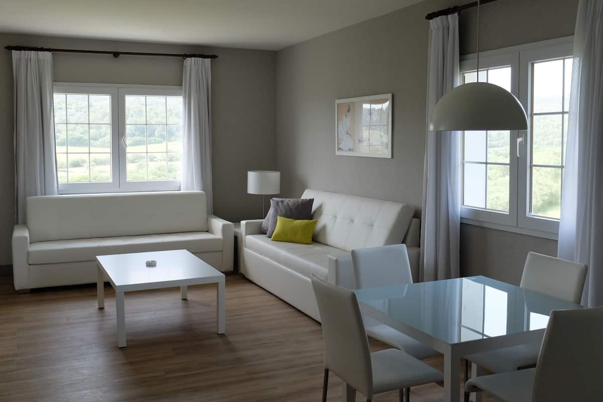 Una sala de estar moderna con un sofá blanco, una mesa de comedor de vidrio y una lámpara.