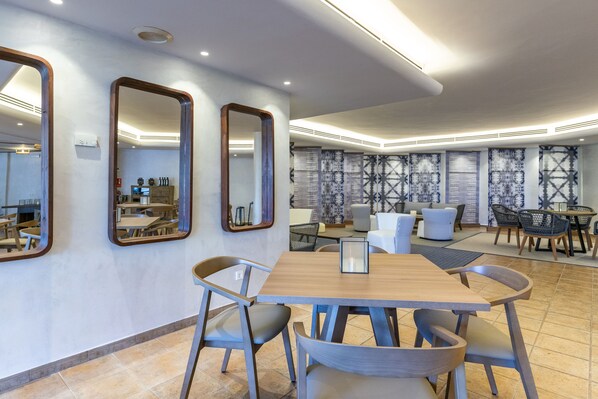 Un comedor moderno con una mesa y sillas de madera, tres espejos en la pared y papel tapiz estampado.