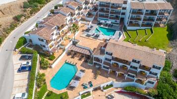 Un hotel de varios pisos con piscina, varios balcones y un estacionamiento.
