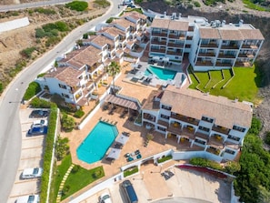 A multi-story hotel with a swimming pool, multiple balconies, and a parking area. - Calallonga Hotel Menorca (Mahón)