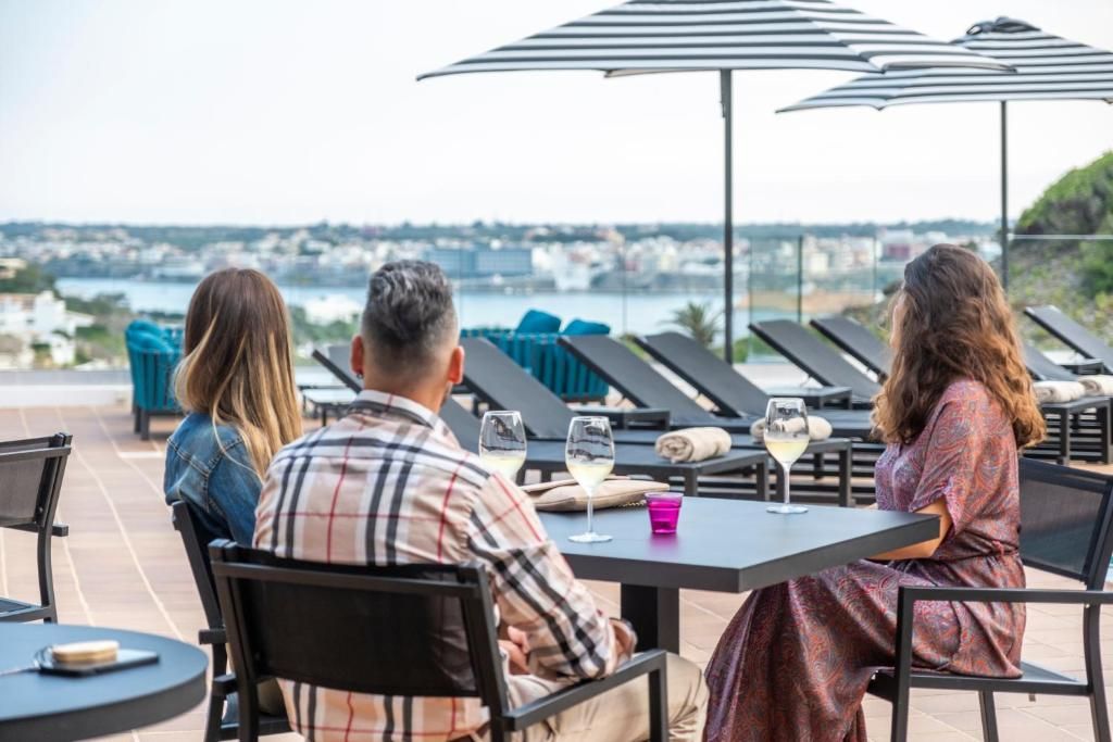 A terrace with tables and chairs, overlooking a body of water and a cityscape.
