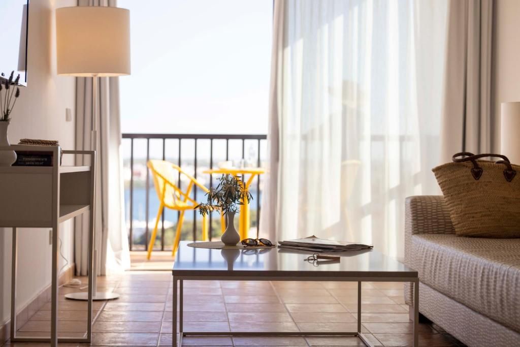 Una sala moderna con una mesa de centro de vidrio, un sofá, una lámpara y vistas a un balcón con sillas amarillas.