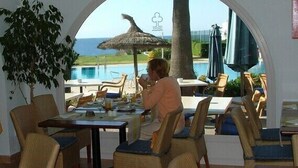 A dining area with a view of the sea, outdoor seating, and a thatched umbrella. - Apartamentos Parque Mar (Santanyi)