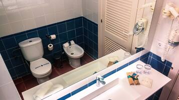 A bathroom with a toilet, bidet, and sink with toiletries.