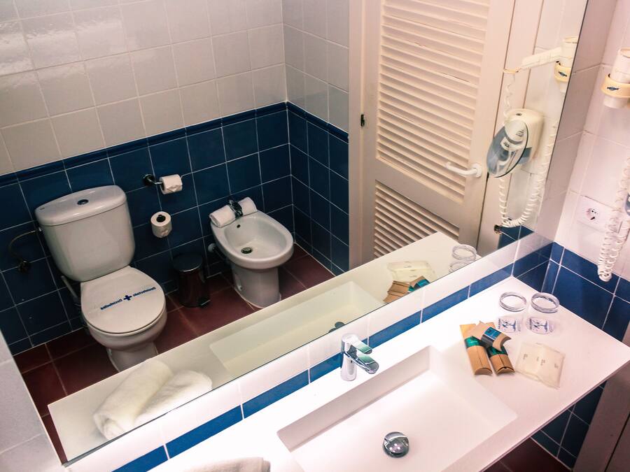 A bathroom with a toilet, bidet, and sink with toiletries.