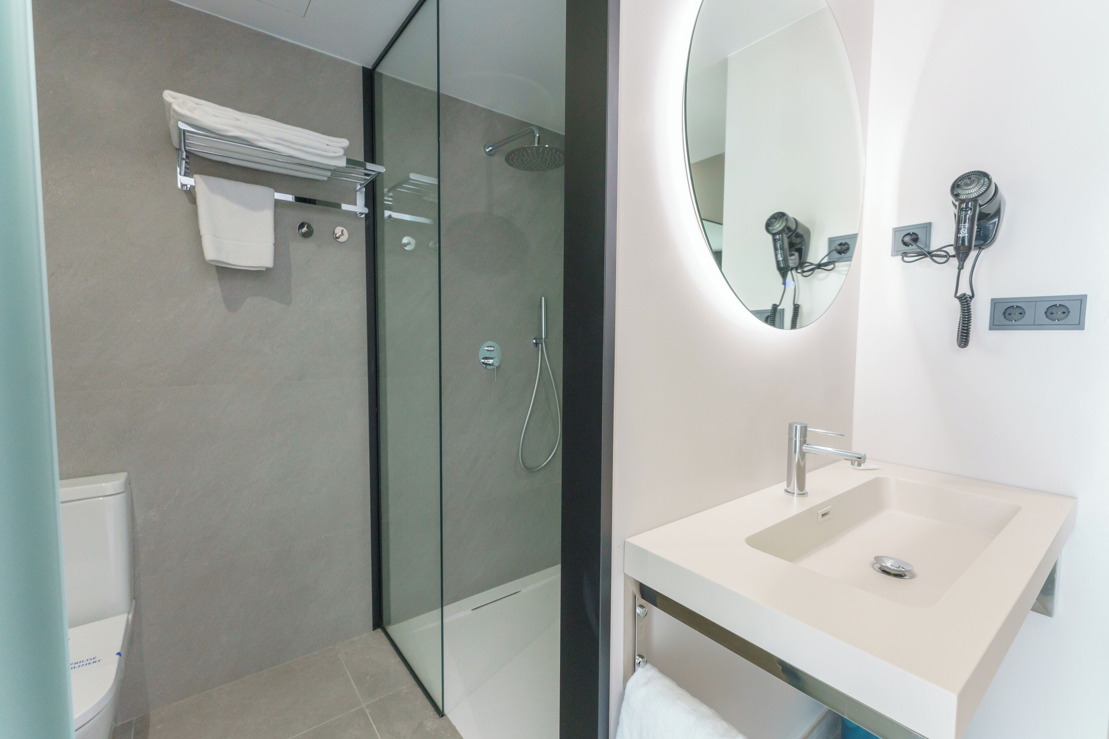 A modern bathroom with a glass-enclosed shower, a white sink, and a hairdryer mounted on the wall.