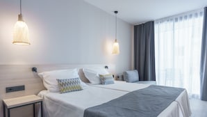 Una habitación de hotel moderna con una cama grande, mesitas de noche y dos lámparas colgantes.