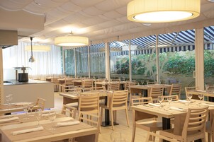 Un restaurante con mesas y sillas de madera, amplios ventanales y lámparas colgantes.