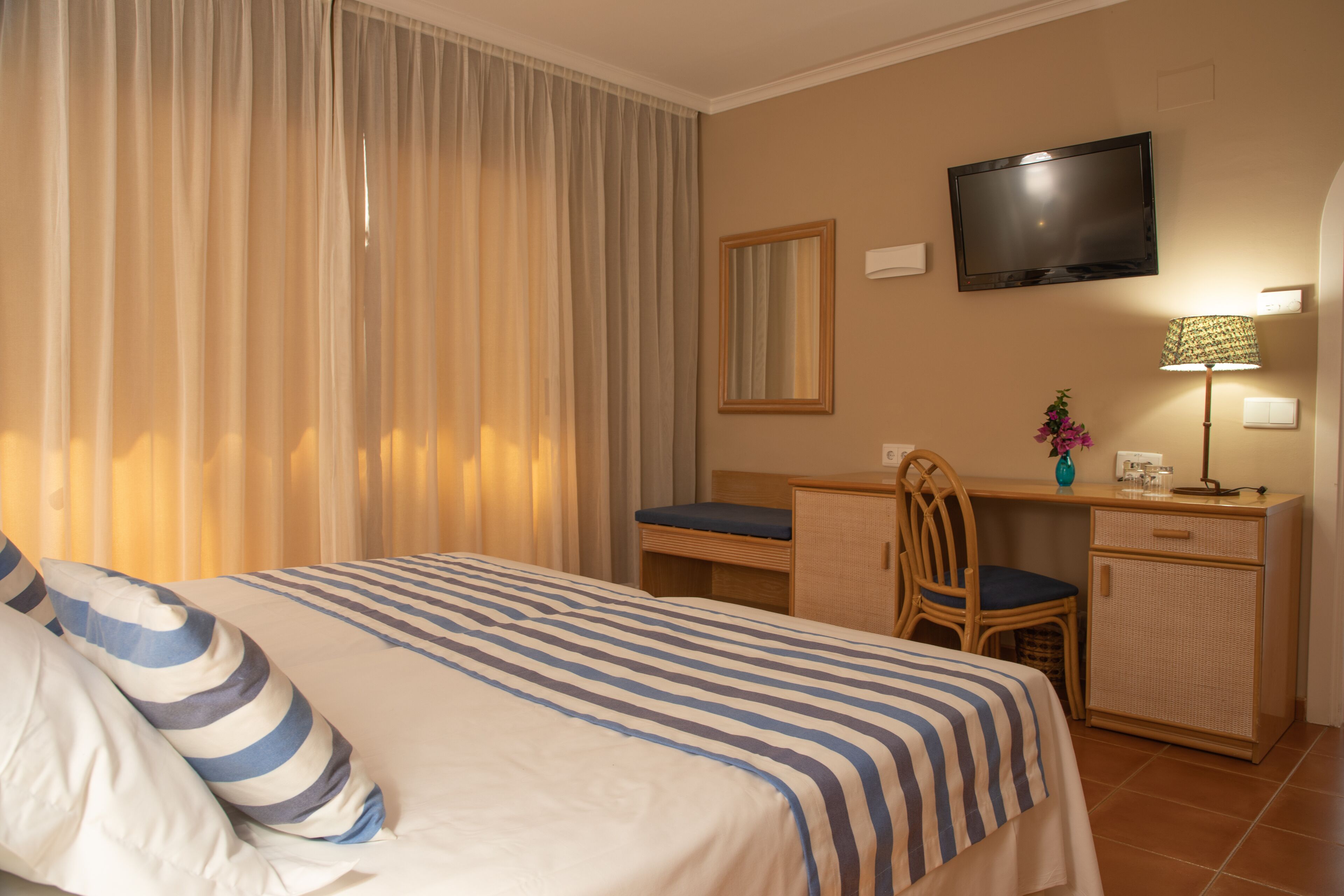A hotel room with a bed, a desk, a chair, a television, and a lamp.