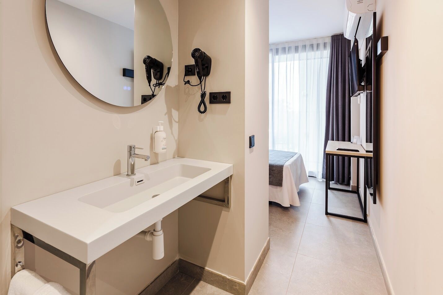 Een moderne badkamer met een grote wastafel, een spiegel en een aan de muur bevestigde haardroger.
