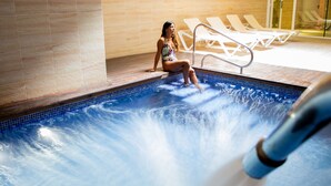Un área de piscina con una persona sentada al borde, sillones de descanso y suelo de baldosas.