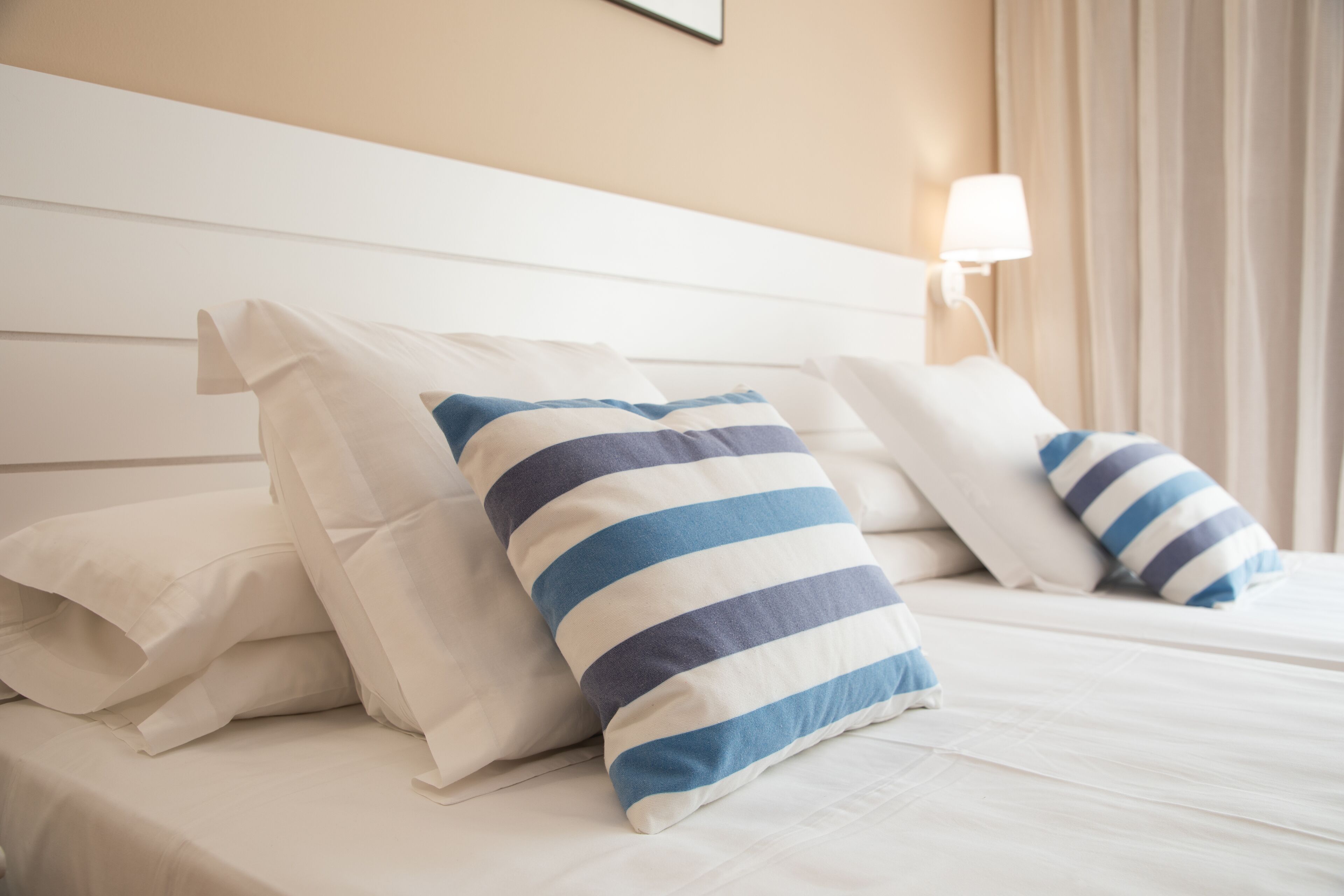 A hotel room with a bed, white bedding, and striped pillows.