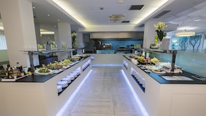 Una moderna barra de buffet con múltiples estaciones de servicio, un mostrador central y vistas al área de cocina al fondo.