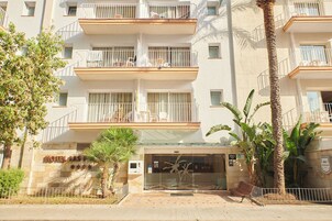 Un hotel con varios balcones, palmeras y una entrada con portón.