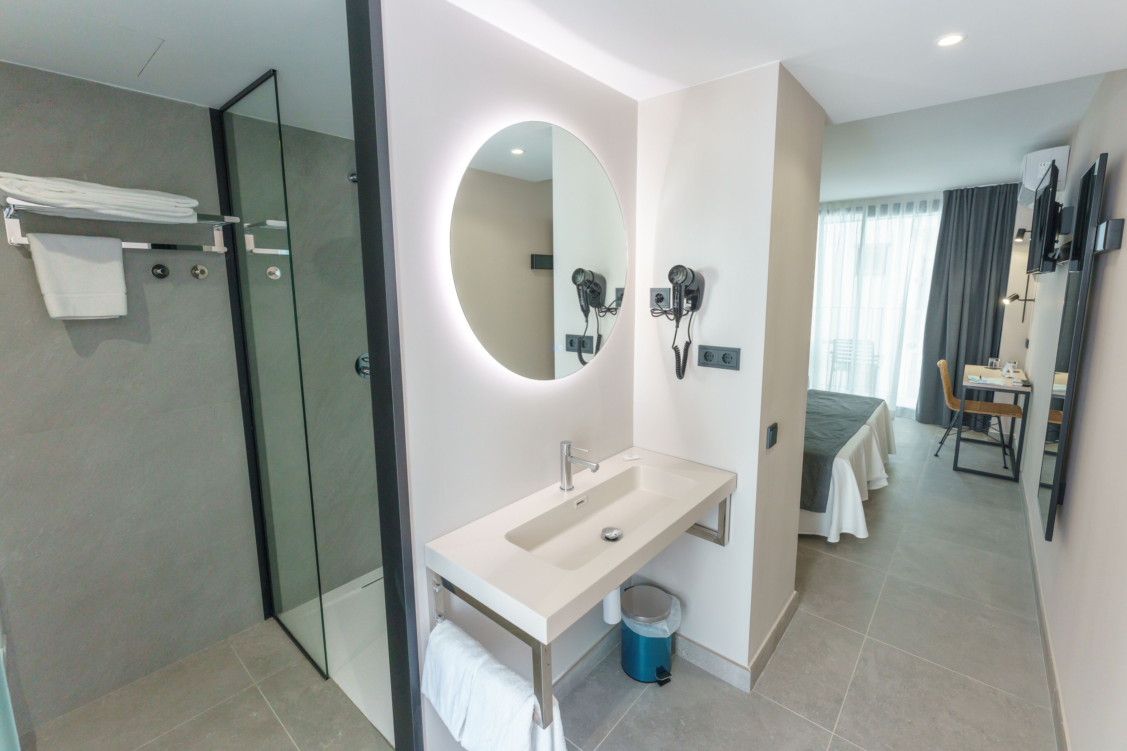 Un baño moderno con cabina de ducha de vidrio, lavabo con espejo y secador de pelo montado en la pared.