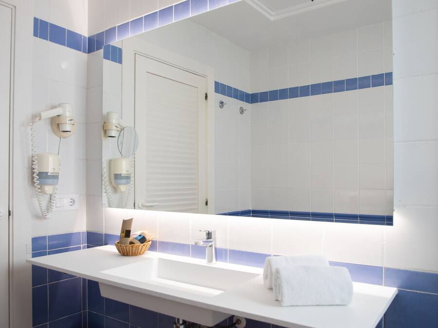 Une salle de bain avec un lavabo blanc, des murs recouverts de carreaux bleus, un grand miroir et un porte-serviettes.