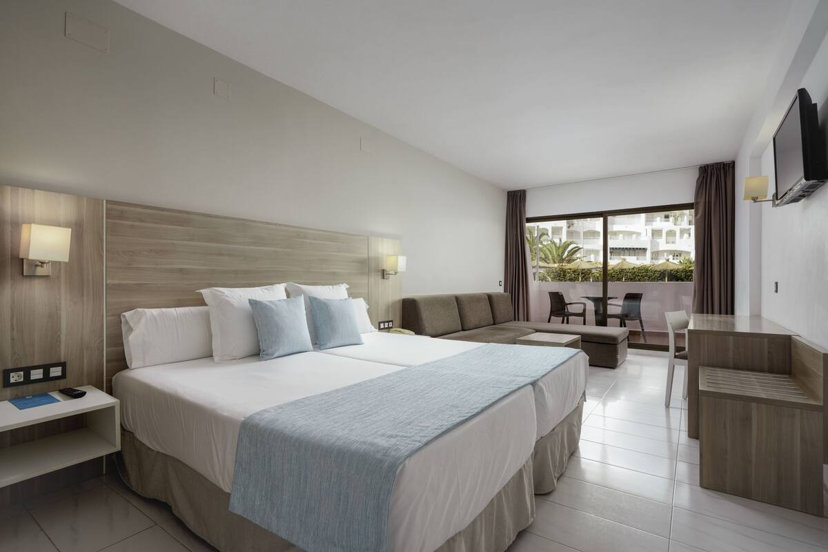 A modern hotel room with a large bed, a sofa, a desk, and a balcony with a view.