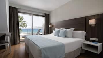 A hotel room with a large bed, a desk, a chair, a nightstand, and a view of the beach.