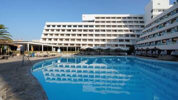 A hotel with a large swimming pool, multiple balconies, and lounge areas.
